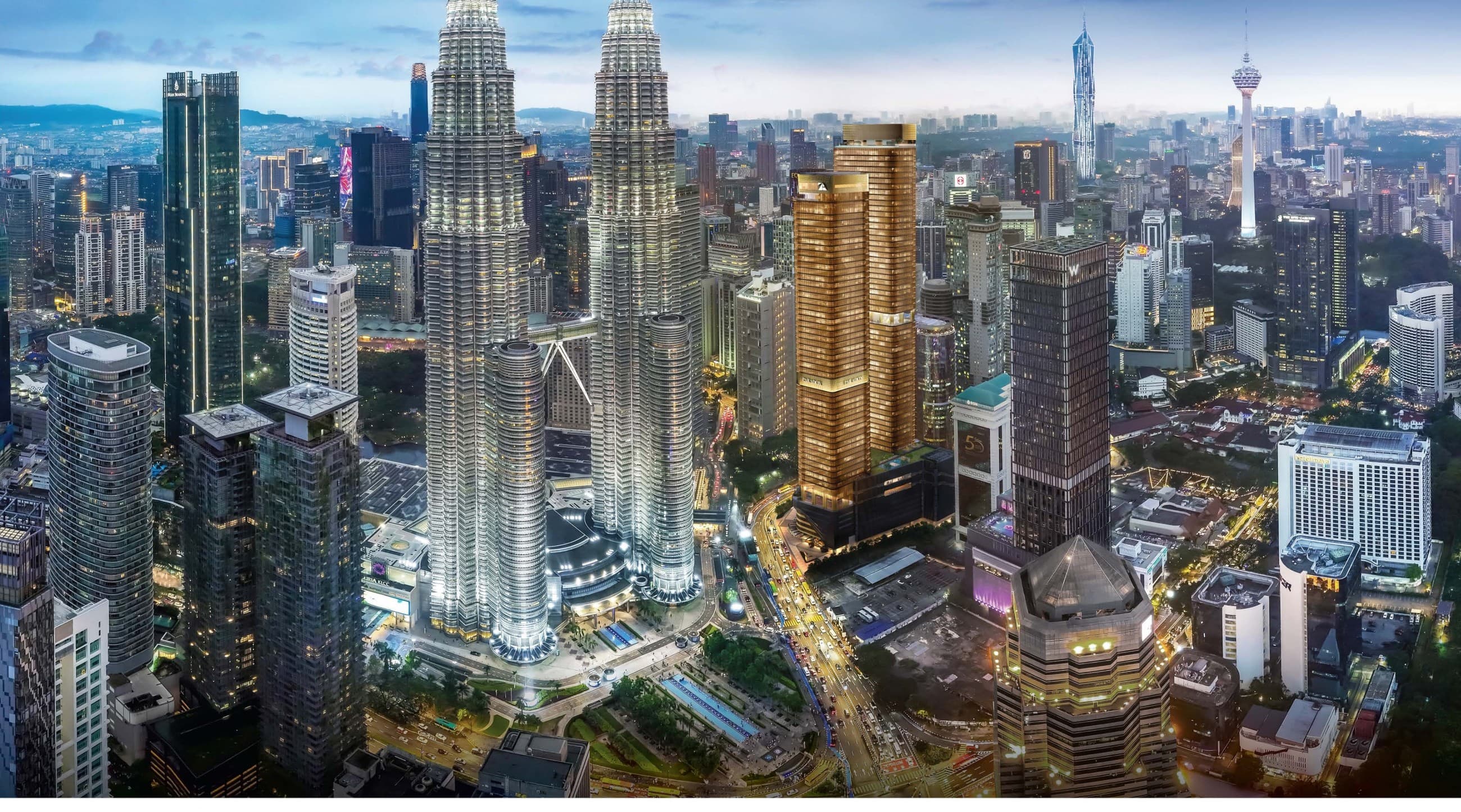 The Kuala Lumpur skyline at dusk from above — the Petronas Twin Towers lit at the centre, Merdeka 118 and the KL Tower on the horizon, and the KLCC precinct below, the panorama the CloutHaus brochure prints as its crown-jewel spread