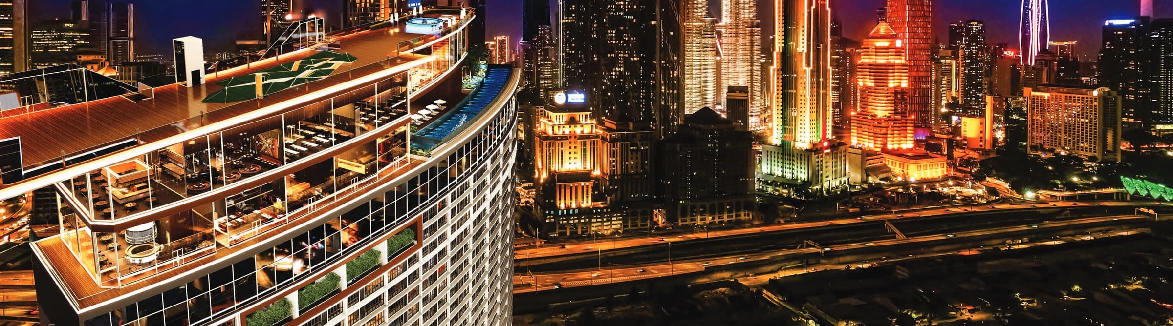 The KL360 Sky Deck at night, the curved deck and pool at the crown of the tower above the lit Kuala Lumpur skyline with the Petronas Twin Towers and Merdeka 118, artist's impression