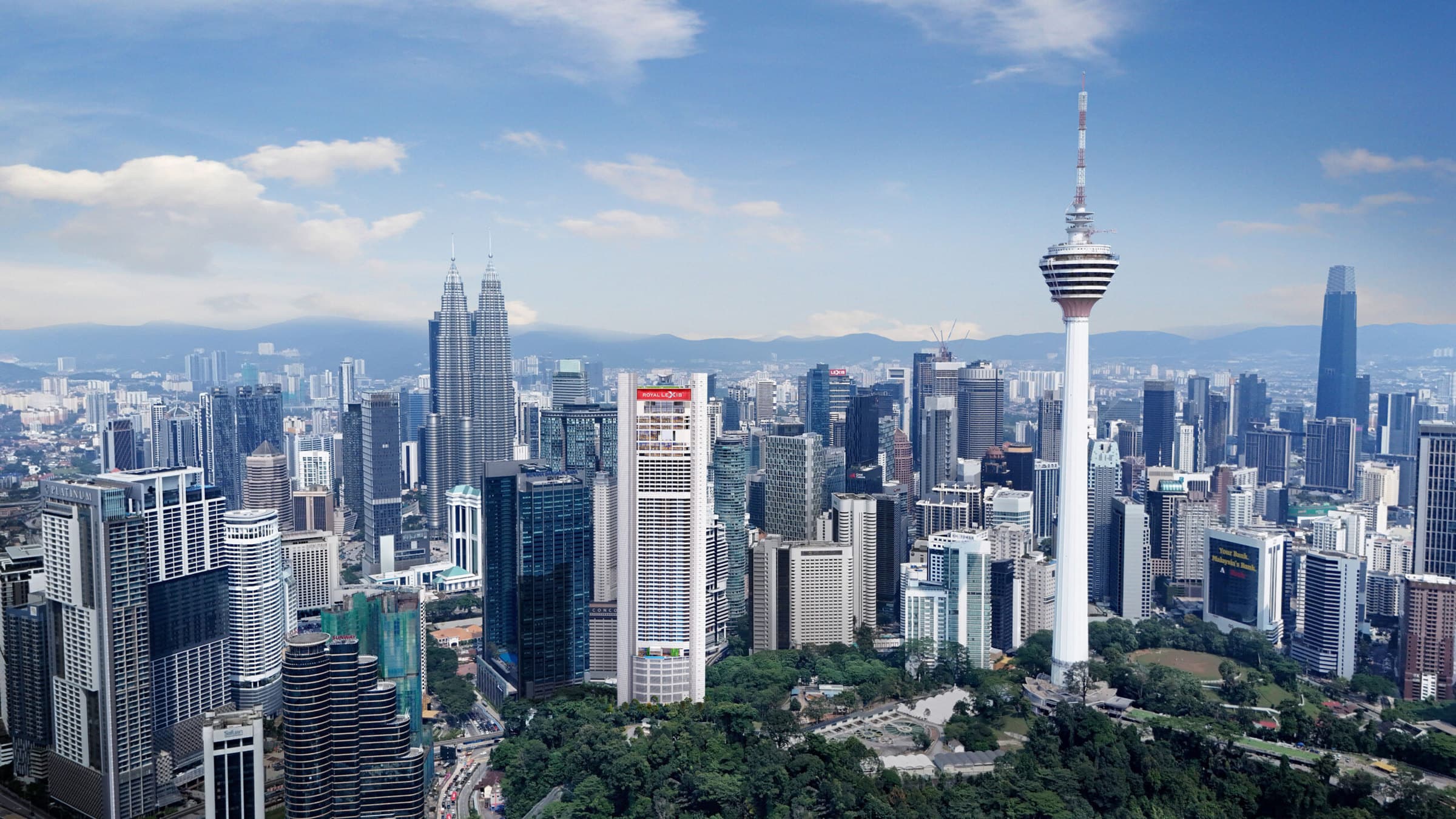 Royal Lexis Kuala Lumpur from the air by day — the white tower on Jalan Sultan Ismail beside the Bukit Nanas forest reserve, with Menara Kuala Lumpur alongside it and the Petronas Twin Towers and Merdeka 118 across the city